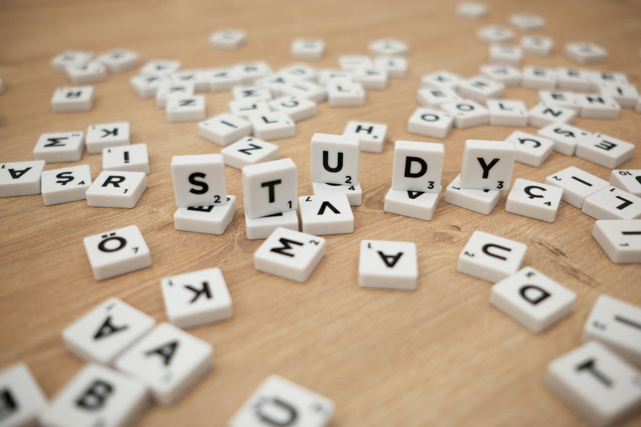 Close-up of letter tiles spelling Study amidst scattered letters on a wooden surface.
